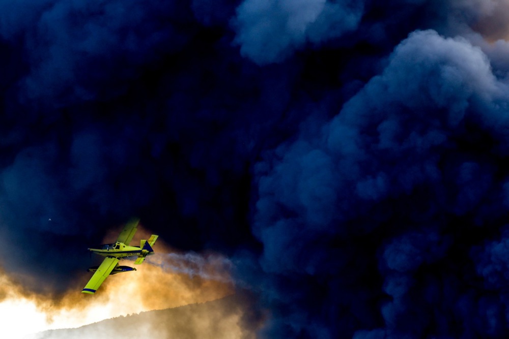 epa12374314 An air tractor aircraft drops water to extinguish a fire at a factory in Trubarevo, on the outskirts of Skopje, North Macedonia, 13 September 2025. A fire broke out on 13 September at a plastics and electronic waste recycling plant in the village of Trubarevo, producing thick black smoke visible from many parts of Skopje. EPA/GEORGI LICOVSKI